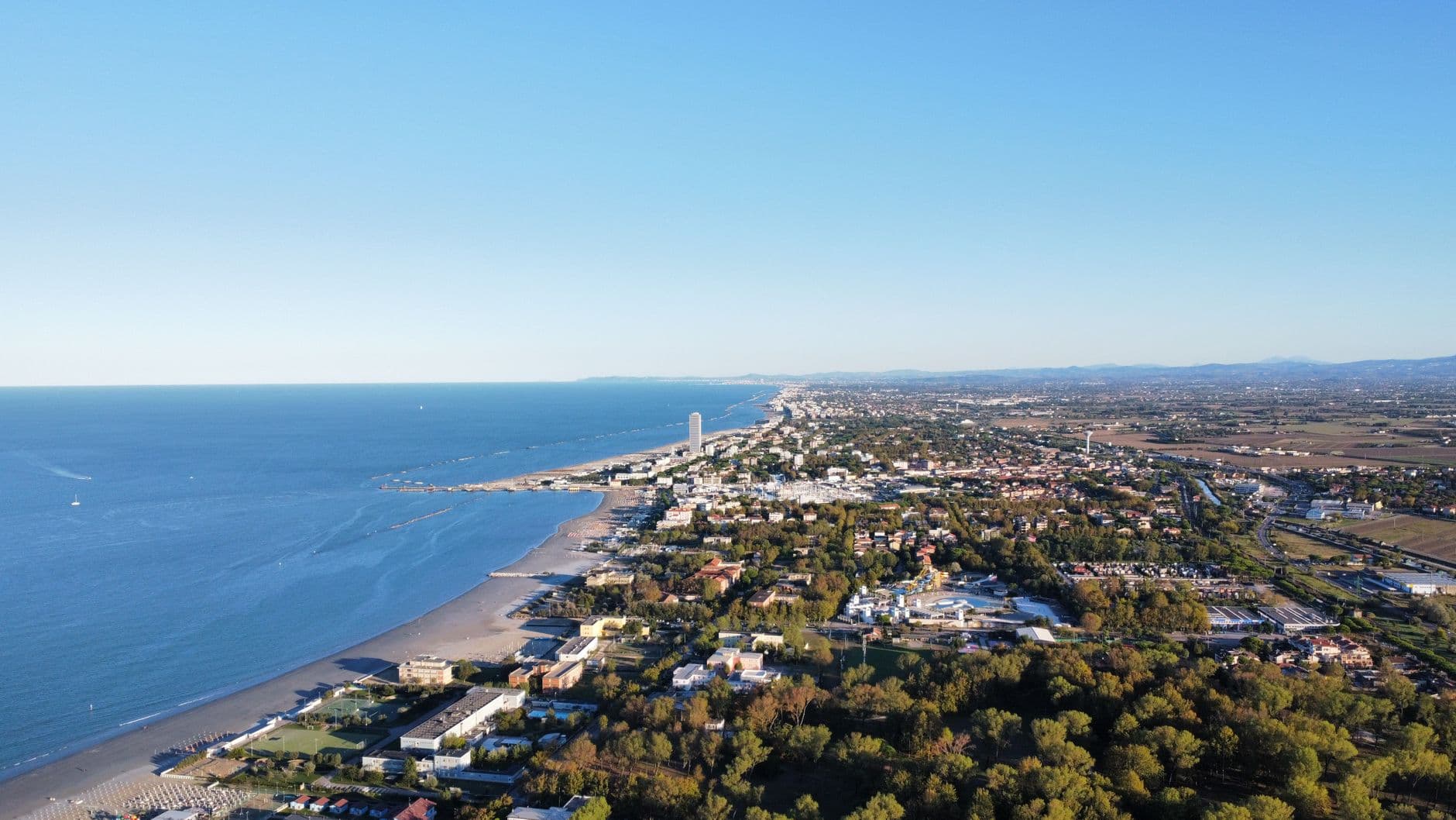 Una vista aérea de una zona residencial moderna y soleada en la costa española con edificios de baja densidad y mucha vegetación.